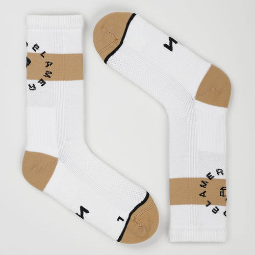 A pair of white padel socks with beige toe and heel sections, a beige horizontal stripe on the cuffs, and black text reading 'PADEL AMERICANO' arranged in a circle. One sock is upright and the other is angled diagonally, set against a clean, light gray background.