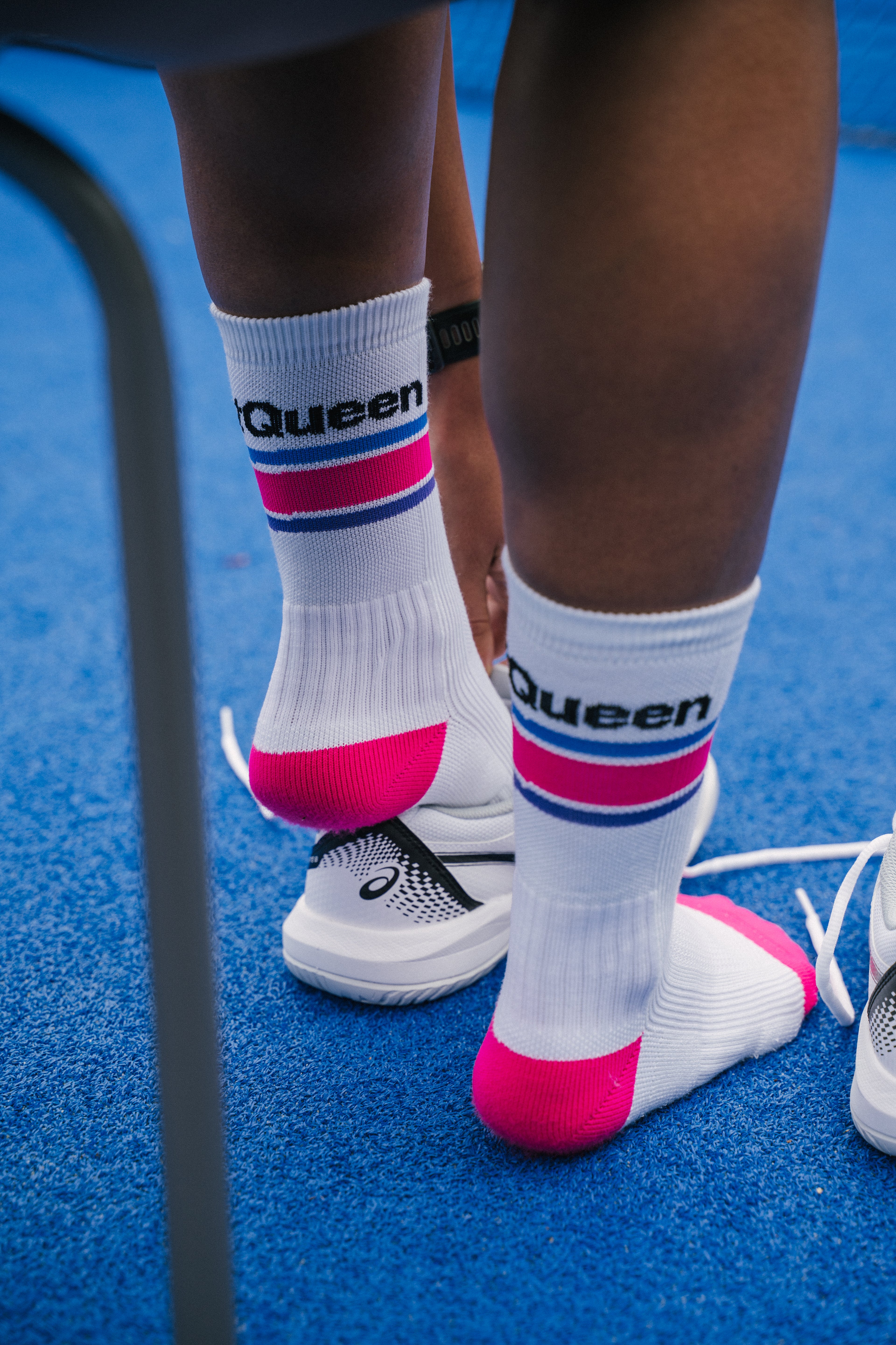 A close-up lifestyle shot on a padel court of a person putting on a white padel shoe while wearing a white NoTennis padel sock with 'Net Queen' printed on it.