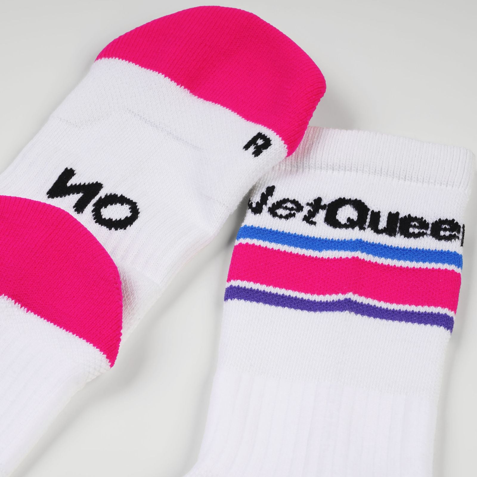 A pair of white padel socks with neon pink toe and heel sections, featuring black knit branding. One sock displays 'NO' and the other shows 'Net Queen' above horizontal stripes in blue, pink, and purple.