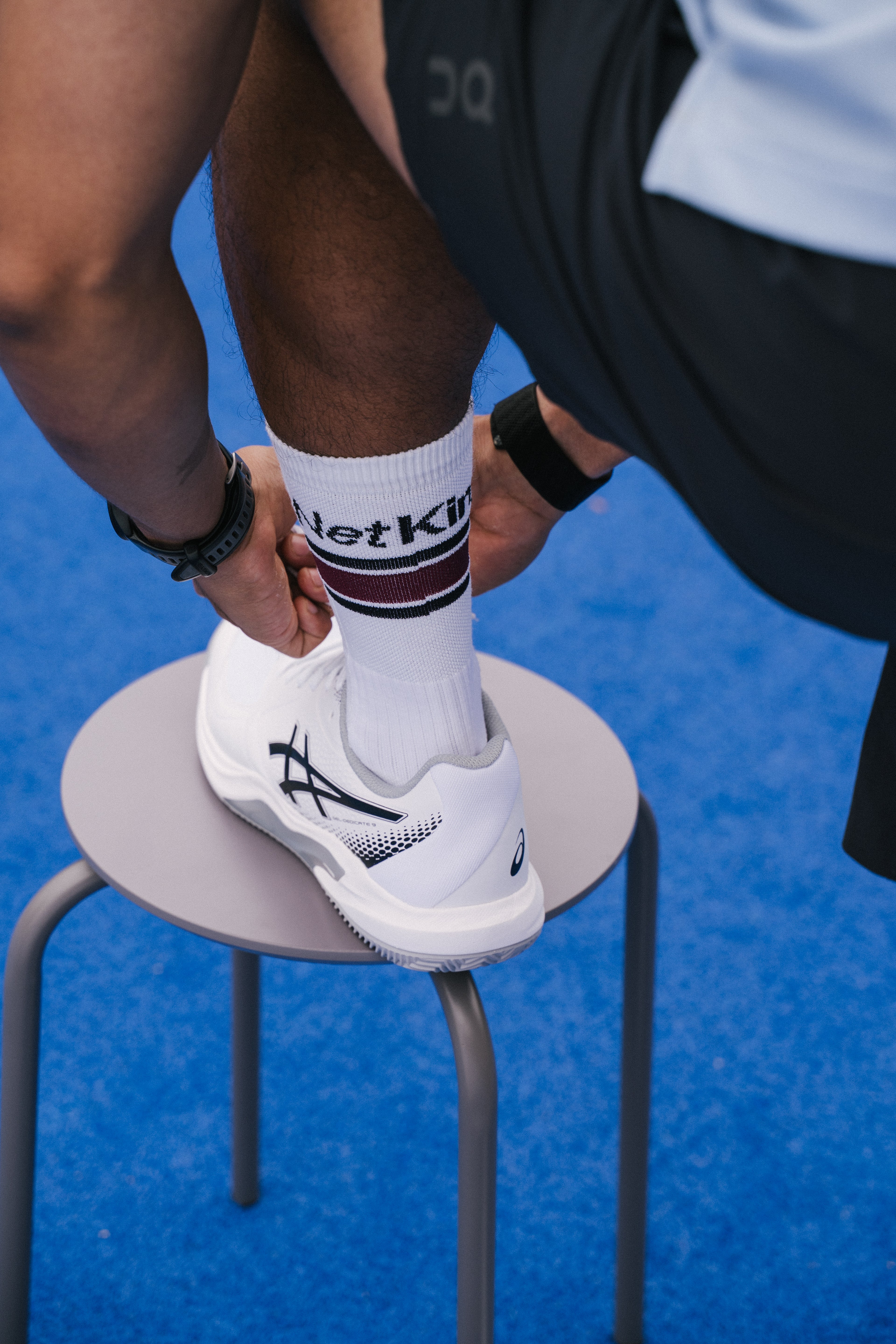A close-up lifestyle shot of a person tying the ankle strap of a white padel shoe while wearing a white NoTennis padel sock with 'Net King' printed on it.