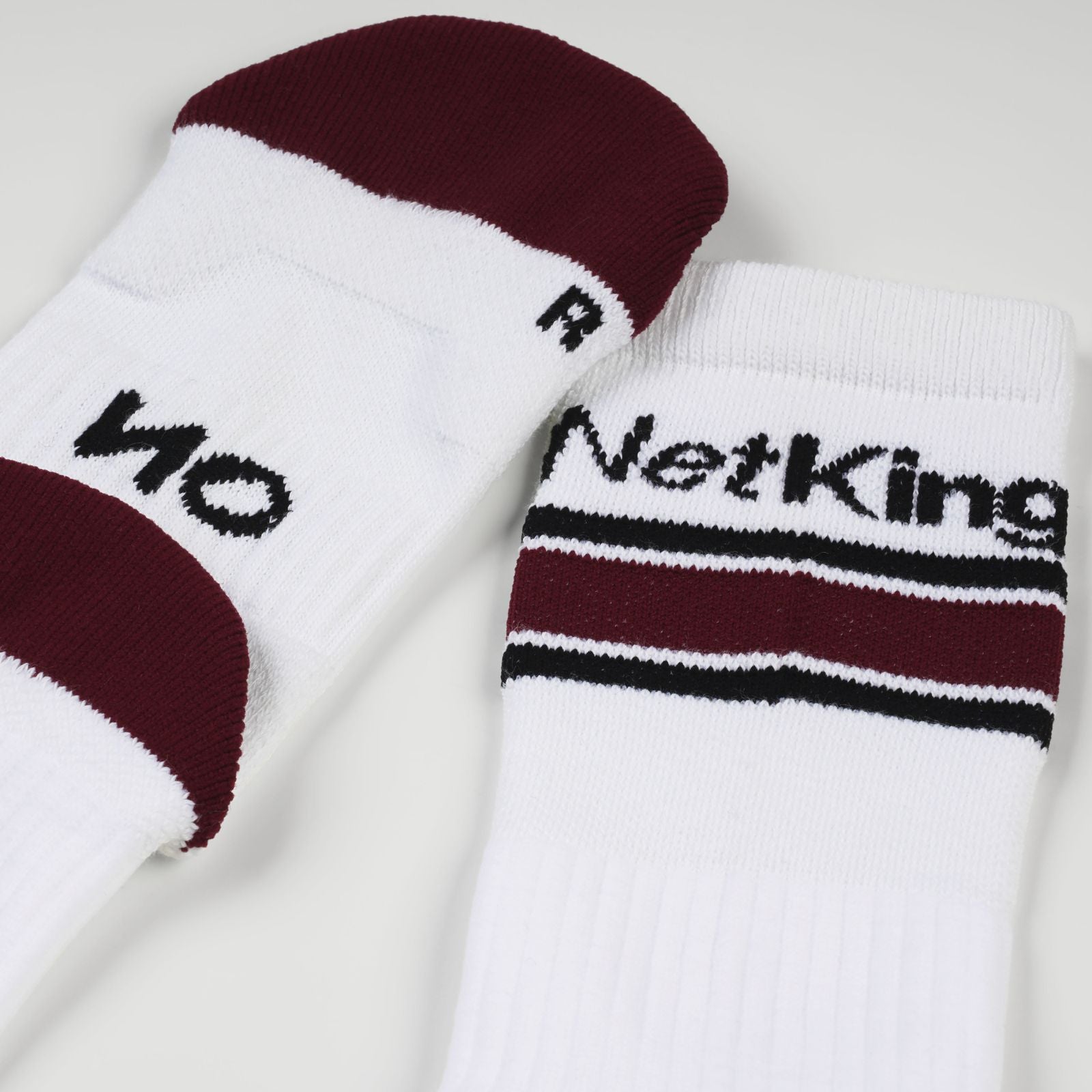A pair of white padel socks with red and black stripes, featuring the brand's NoTennis padel sock 'Net King' and 'NO' printed on them, set against a plain light background.